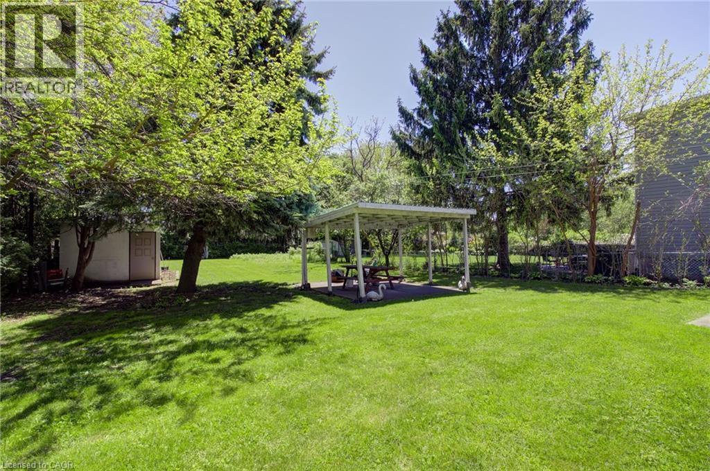 Spacious rear yard featuring an open-sided covered patio, mature trees providing natural shade, a storage shed, and a verdant lawn - 2344 Brinell Avenue, Burlington, ON - Outdoor