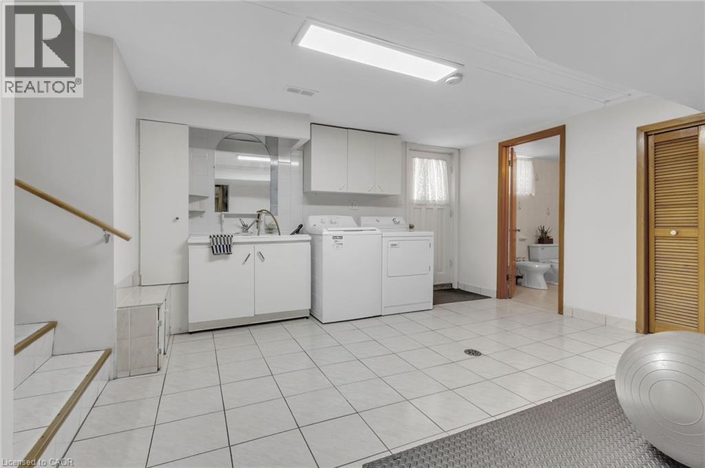 Tiled flooring throughout a utility space featuring a laundry area with built-in cabinetry, a utility sink, and a washer and dryer - 2344 Brinell Avenue, Burlington, ON - Indoor Photo Showing Laundry Room