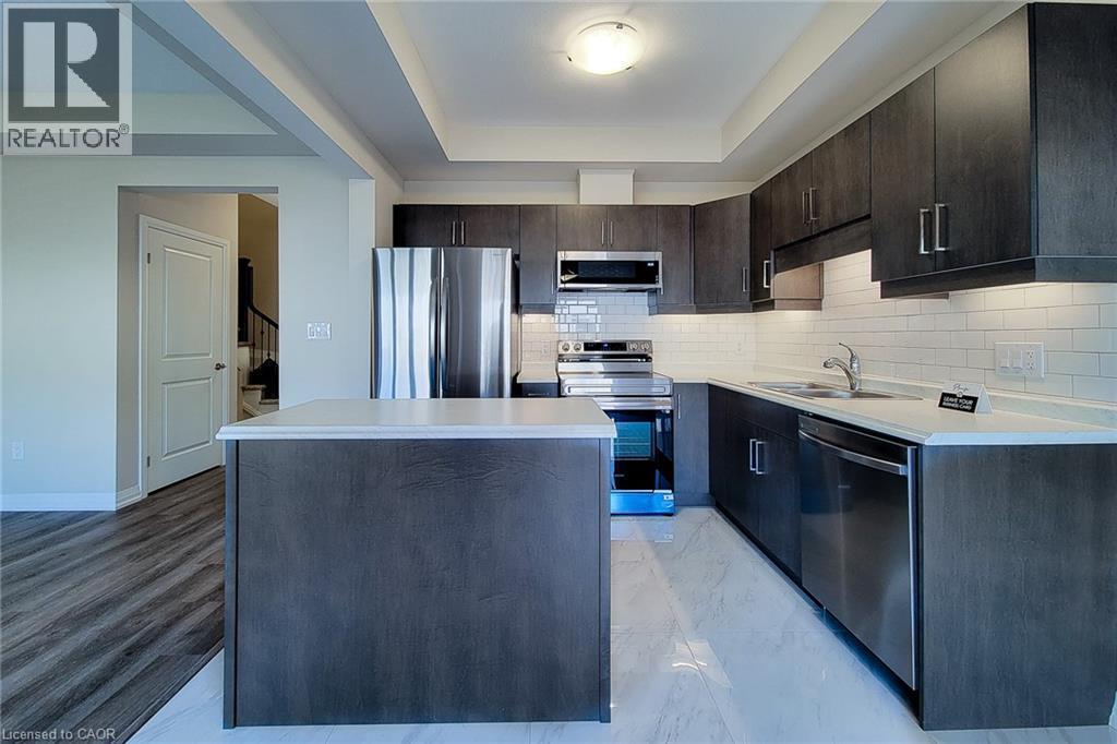 Kitchen featuring dark wood-finish cabinetry, stainless steel appliances, a white subway tile backsplash, and a central island with a light-colored countertop - 111 Alicia Crescent, Thorold, ON