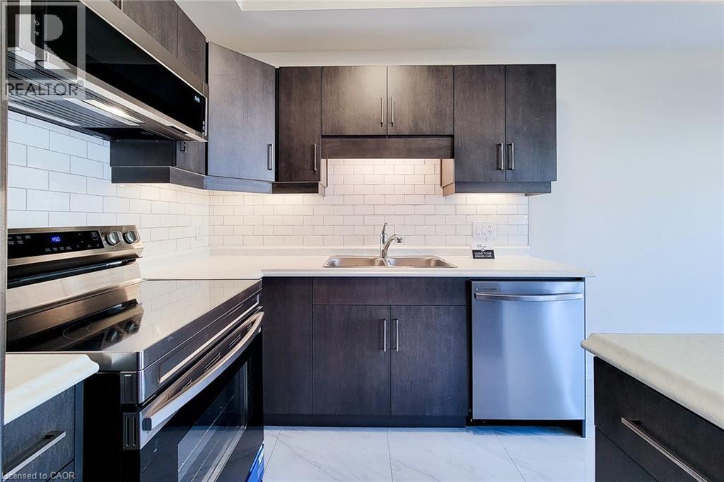 Modern kitchen featuring dark wood-finish cabinetry, stainless steel appliances, white subway tile backsplash, light countertops, and under-cabinet lighting - 111 Alicia Crescent, Thorold, ON