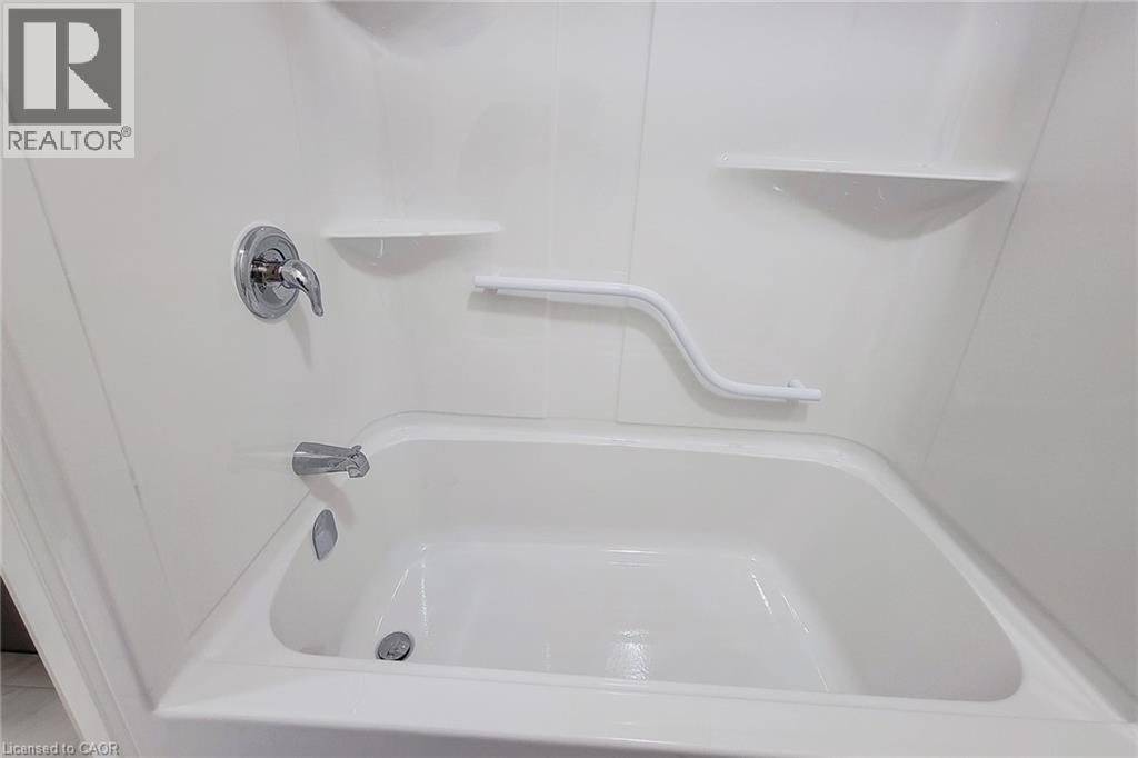 White tub and shower combination with chrome fixtures, integrated shelving, and a safety grab bar - 111 Alicia Crescent, Thorold, ON