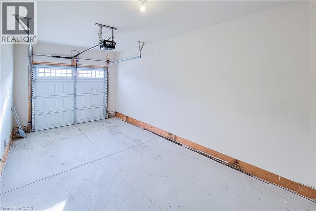 Single-bay garage featuring a concrete floor, white walls, an automatic overhead door opener, and a panel-style garage door with upper window inserts - 111 Alicia Crescent, Thorold, ON