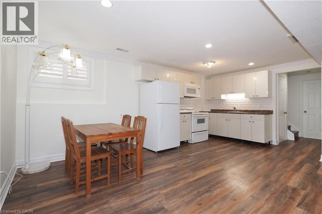 Open-concept kitchen and dining area featuring wood-finish flooring, white cabinetry, integrated appliances, a subway tile backsplash, and recessed lighting - 67 Hollyridge Crescent Unit# Lower, Kitchener, ON - Indoor