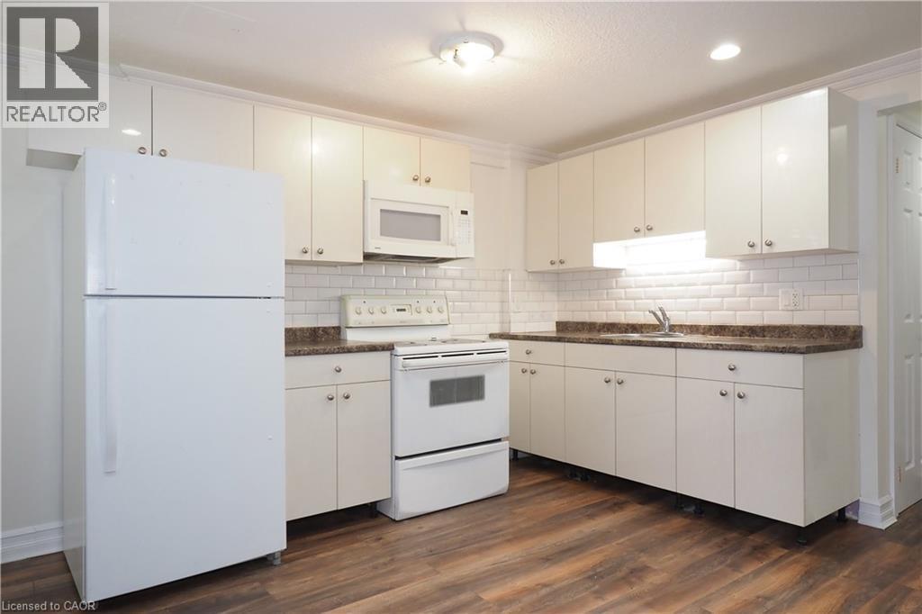 Kitchen featuring wood-finish flooring, white cabinetry, dark stone-look countertops, and a subway tile backsplash - 67 Hollyridge Crescent Unit# Lower, Kitchener, ON - Indoor Photo Showing Kitchen With Double Sink