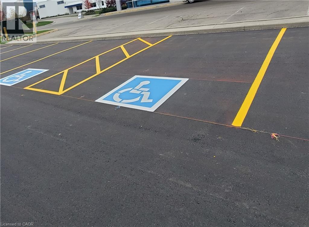 Paved parking lot featuring designated accessible parking spaces with blue and white markings, bright yellow striping, and a concrete curb - 44 Ditton Drive Unit# 3, Hamilton, ON