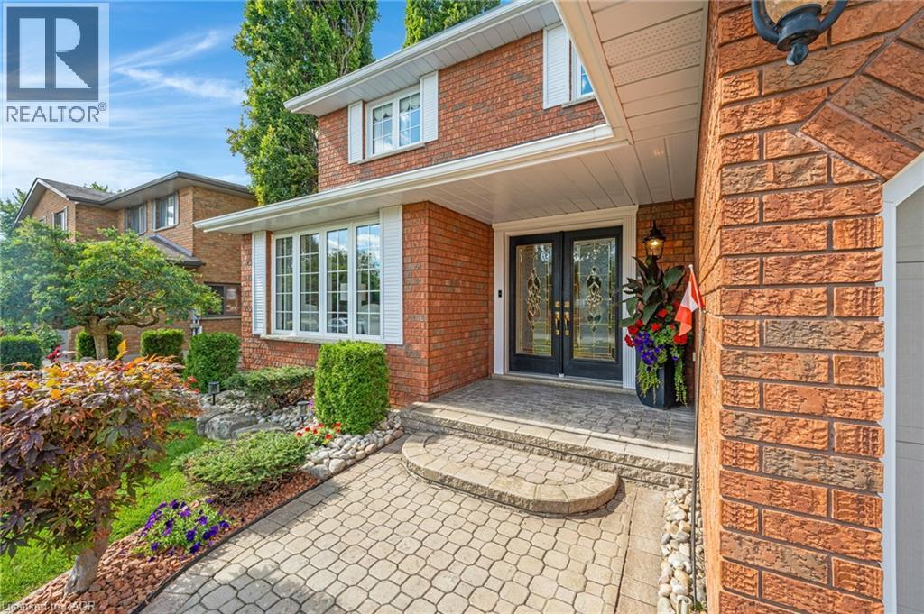 Brick exterior featuring a bay window with white shutters, a paver stone walkway, and a covered entry with double front doors - 228 Michener Crescent, Kitchener, ON - Outdoor
