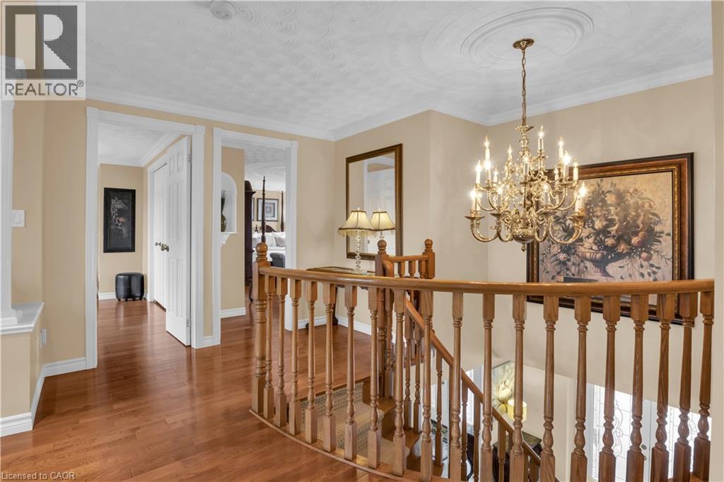Upper landing featuring wood-finish flooring, a brass multi-tier chandelier with ceiling medallion, and a wood banister with traditional balusters - 228 Michener Crescent, Kitchener, ON - Indoor Photo Showing Other Room