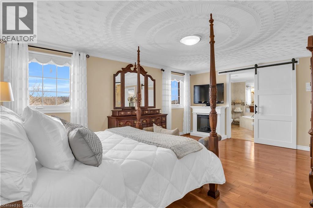 Hardwood flooring throughout featuring a decorative ceiling medallion, an integrated electric fireplace, and a sliding barn door - 228 Michener Crescent, Kitchener, ON - Indoor Photo Showing Bedroom