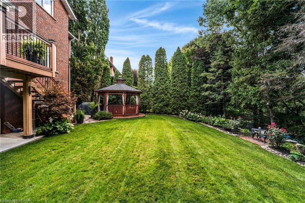 Expansive backyard featuring a manicured lawn, a wooden gazebo with white privacy curtains, mature evergreen trees, and a terraced garden with established plantings - 228 Michener Crescent, Kitchener, ON - Outdoor