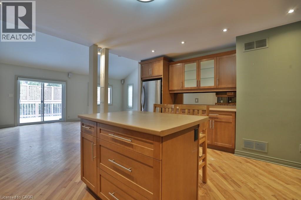 Kitchen island with light-toned countertop and wood-finish cabinetry, stainless steel refrigerator, and wood-finish flooring - 7 Gibson Place Unit# 21, St. Catharines, ON - Indoor Photo Showing Kitchen