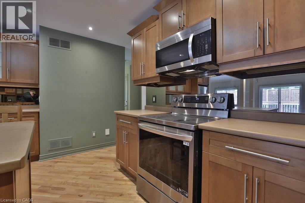 Kitchen featuring stainless steel appliances, wood cabinetry, light-toned countertops, and wood-finish flooring - 7 Gibson Place Unit# 21, St. Catharines, ON - Indoor Photo Showing Kitchen