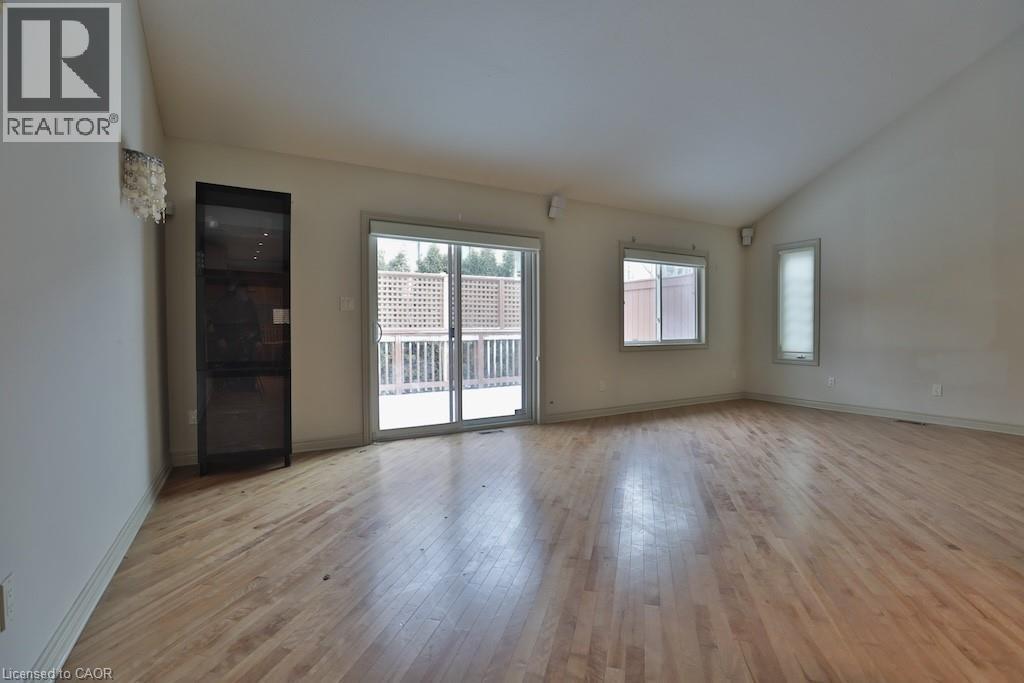 Spacious room featuring wood-finish flooring, vaulted ceiling, built-in display cabinet, and sliding glass doors opening to an exterior deck - 7 Gibson Place Unit# 21, St. Catharines, ON - Indoor Photo Showing Other Room