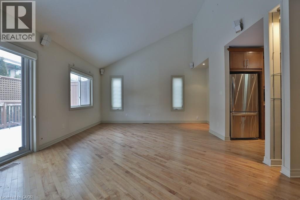 Vaulted ceiling great room with wood-finish flooring, two windows, and a sliding glass door leading to a wood deck - 7 Gibson Place Unit# 21, St. Catharines, ON - Indoor Photo Showing Other Room