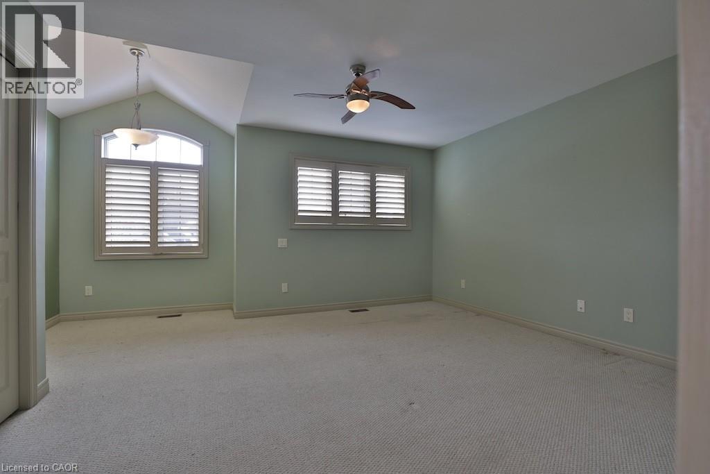 Carpeted room featuring a vaulted ceiling with a pendant light fixture, a second ceiling fan with integrated lighting, and two windows equipped with louvered shutters - 7 Gibson Place Unit# 21, St. Catharines, ON - Indoor Photo Showing Other Room