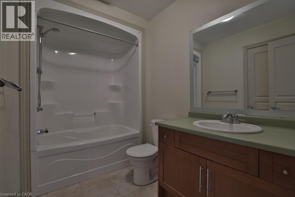 Bathroom featuring a white bathtub and shower combination with an integrated showerhead, a toilet, and a wood-finish vanity with a green countertop and an undermount sink - 7 Gibson Place Unit# 21, St. Catharines, ON - Indoor Photo Showing Bathroom