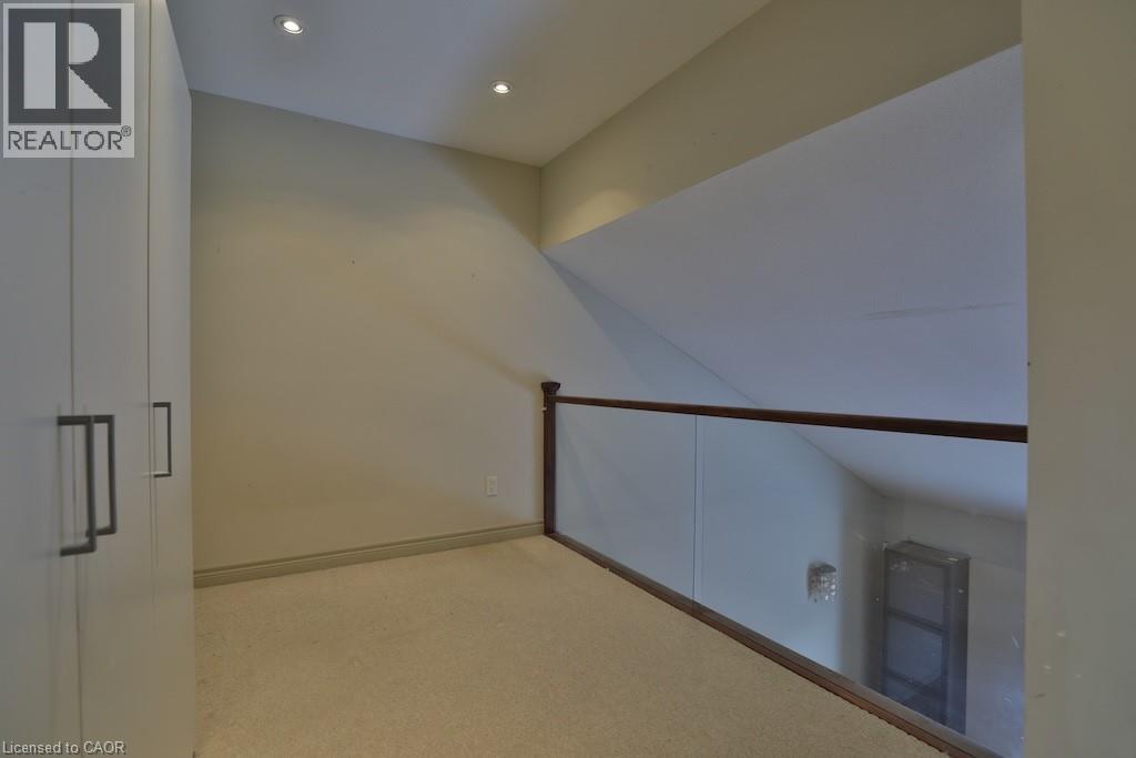 Carpeted loft area featuring built-in cabinetry with contemporary hardware, recessed lighting, and a glass-paneled railing with a wood-finish top rail - 7 Gibson Place Unit# 21, St. Catharines, ON - Indoor Photo Showing Other Room