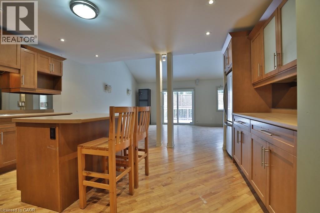 Kitchen and living area featuring wood-finish flooring, light wood cabinetry with frosted glass accents, and a built-in breakfast bar - 7 Gibson Place Unit# 21, St. Catharines, ON - Indoor Photo Showing Kitchen