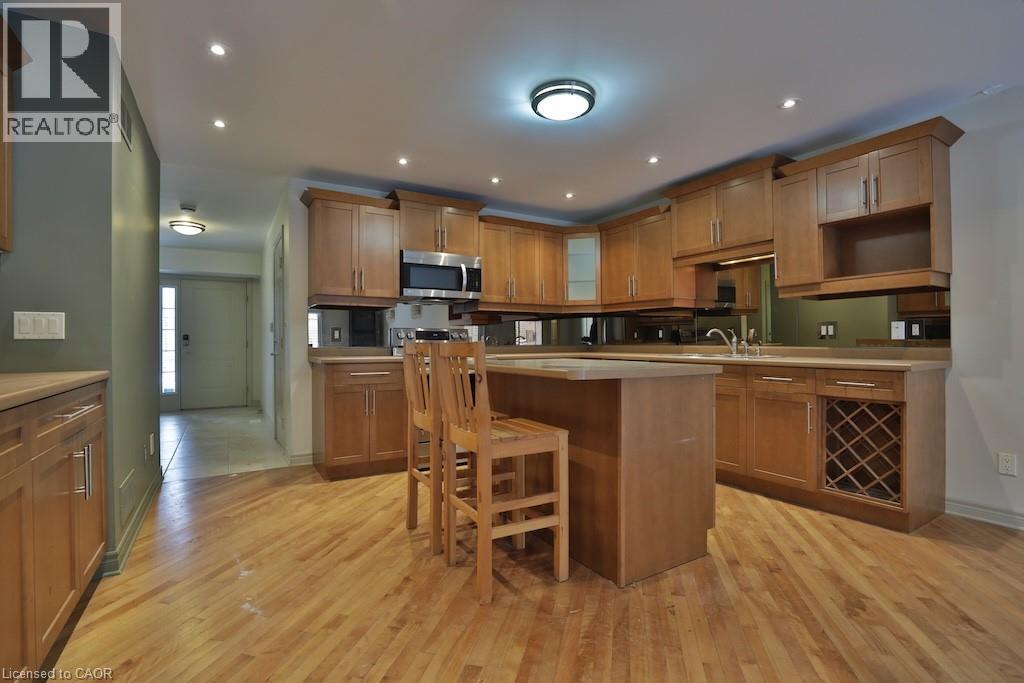 Hardwood flooring throughout the kitchen featuring abundant wood cabinetry, stainless steel microwave, integrated wine rack, and recessed lighting - 7 Gibson Place Unit# 21, St. Catharines, ON - Indoor Photo Showing Kitchen