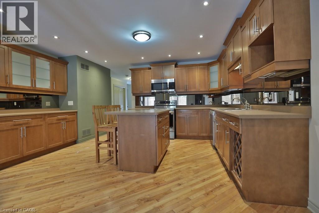 Kitchen featuring wood-finish flooring, recessed lighting, wood cabinetry with glass-front accents, a central island, and stainless steel appliances - 7 Gibson Place Unit# 21, St. Catharines, ON - Indoor Photo Showing Kitchen