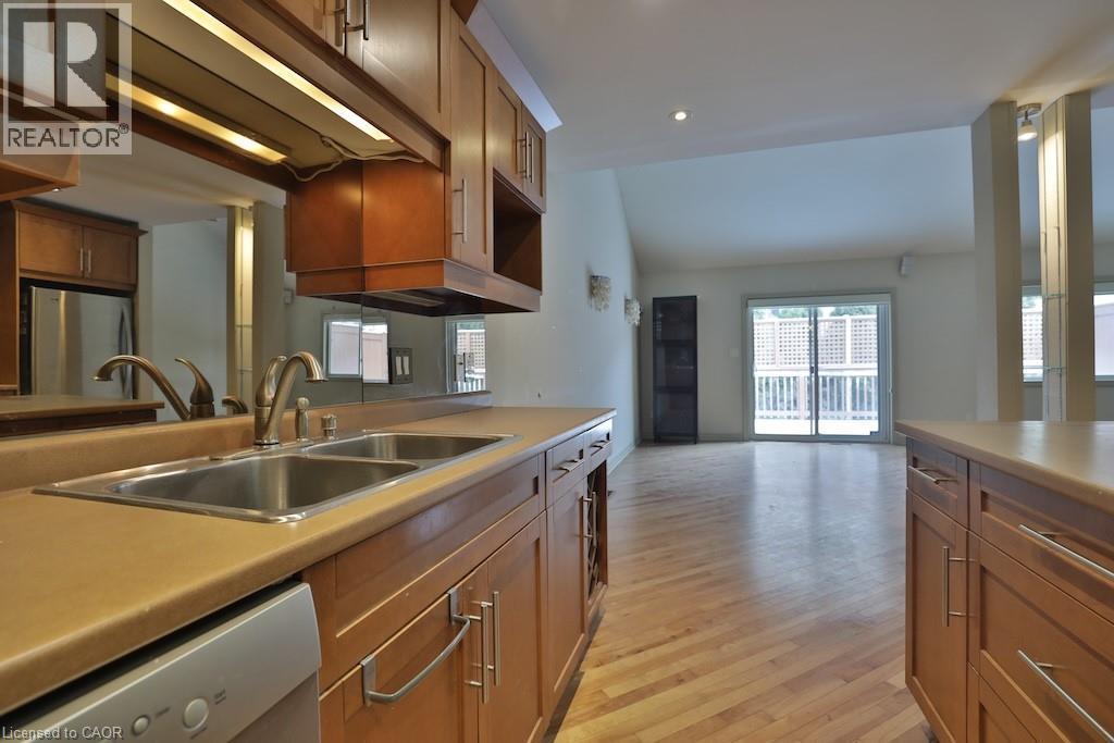 Kitchen featuring wood cabinetry, a double basin stainless steel sink, and light-toned countertops - 7 Gibson Place Unit# 21, St. Catharines, ON - Indoor Photo Showing Kitchen With Double Sink