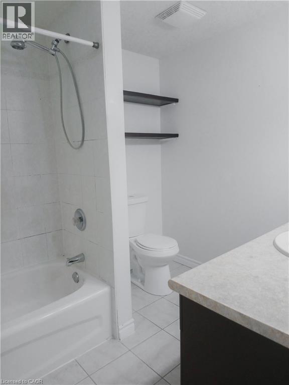 Bathroom featuring a white tub with tiled surround, a toilet, a dark wood-finish vanity with light-toned countertop, and light-toned floor tiling - 569 Activa Avenue, Kitchener, ON - Indoor Photo Showing Bathroom