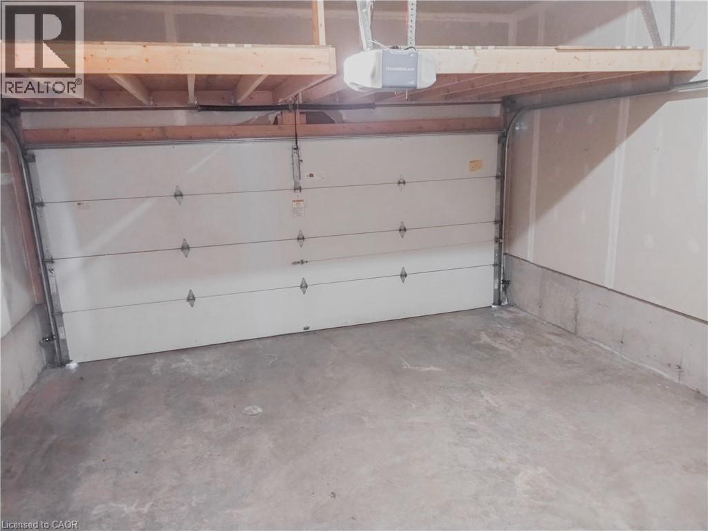 Interior garage space featuring a white sectional garage door, concrete flooring, and an overhead storage platform - 569 Activa Avenue, Kitchener, ON - Indoor Photo Showing Garage