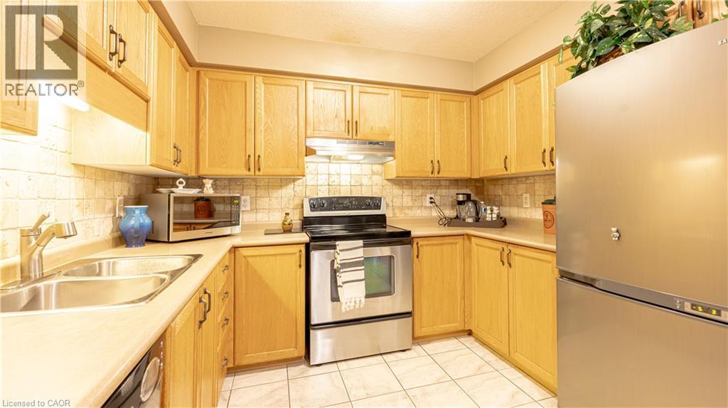Kitchen with under cabinet range hood, stainless steel appliances, a sink, light countertops, and decorative backsplash - 85 Bankside Drive Unit# E34, Kitchener, ON - Indoor Photo Showing Kitchen With Double Sink