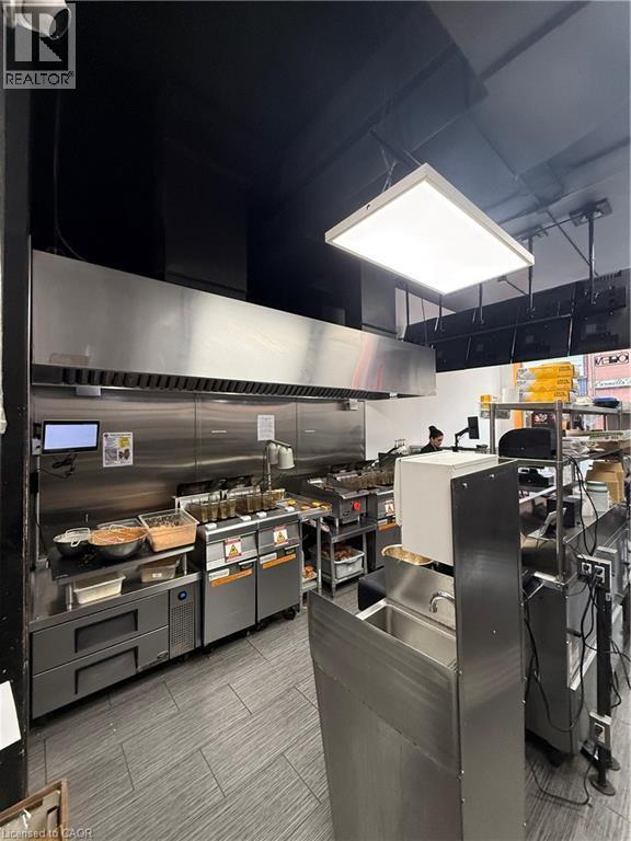 Commercial kitchen featuring a large stainless steel exhaust hood and a suspended rectangular light fixture - 85 King Street W, Kitchener, ON