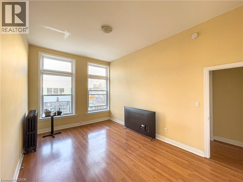 Living area featuring expansive windows, wood-finish flooring, and a classic cast iron radiator - 85 King Street W, Kitchener, ON