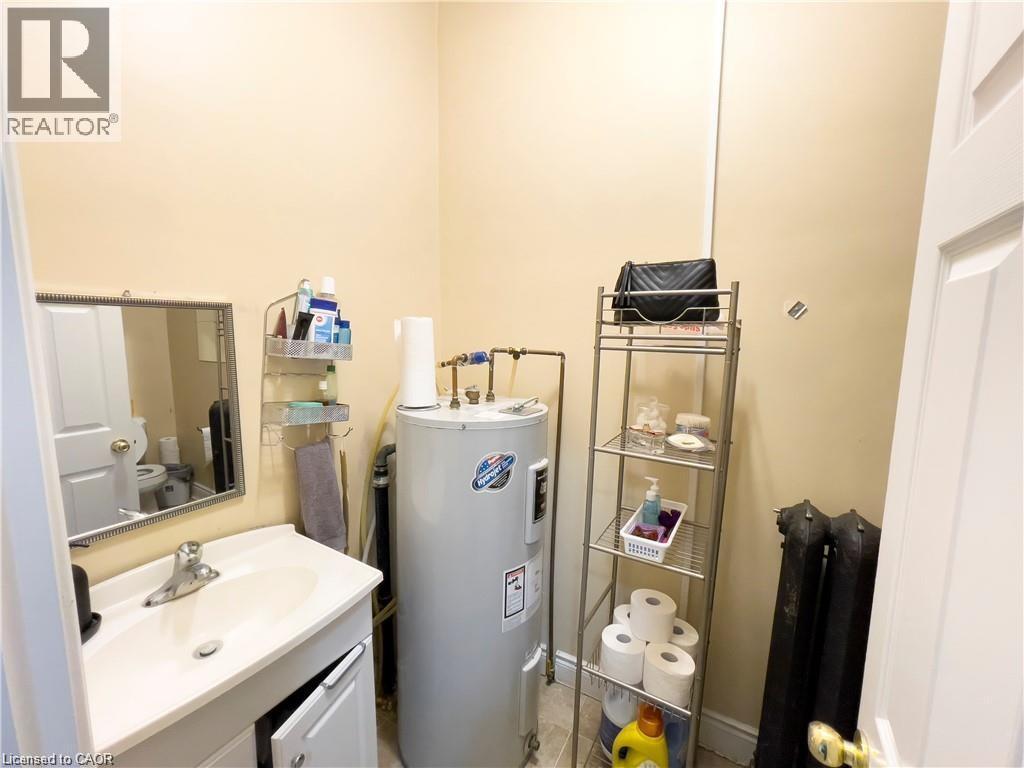Compact utility area featuring a water heater, a white vanity with an integrated sink, and an exposed cast iron radiator - 85 King Street W, Kitchener, ON