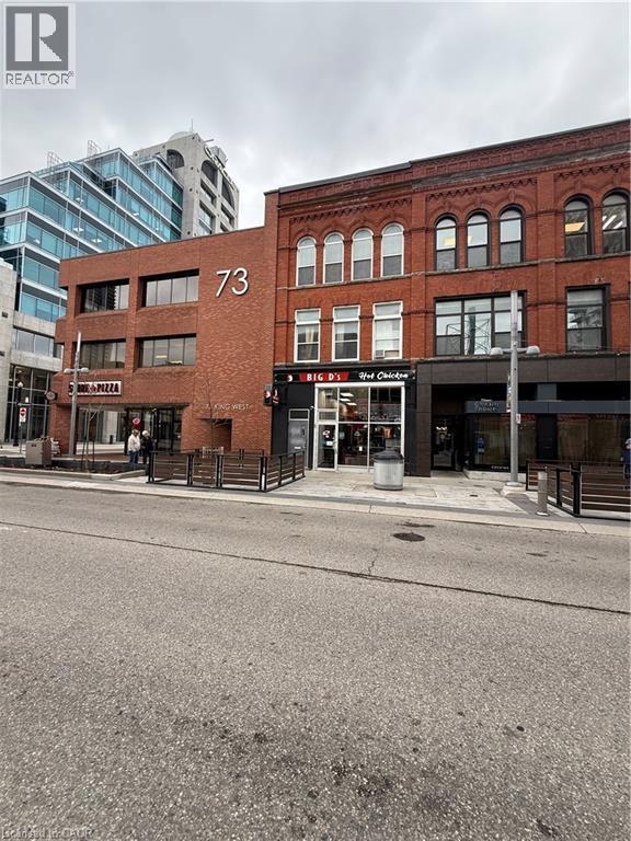 Brick commercial building featuring multiple storefronts, arched windows on upper levels, and a modern adjacent structure - 85 King Street W, Kitchener, ON