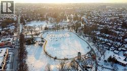 Expansive snow-covered parkland featuring a winding pathway, numerous trees, and a central tower structure -