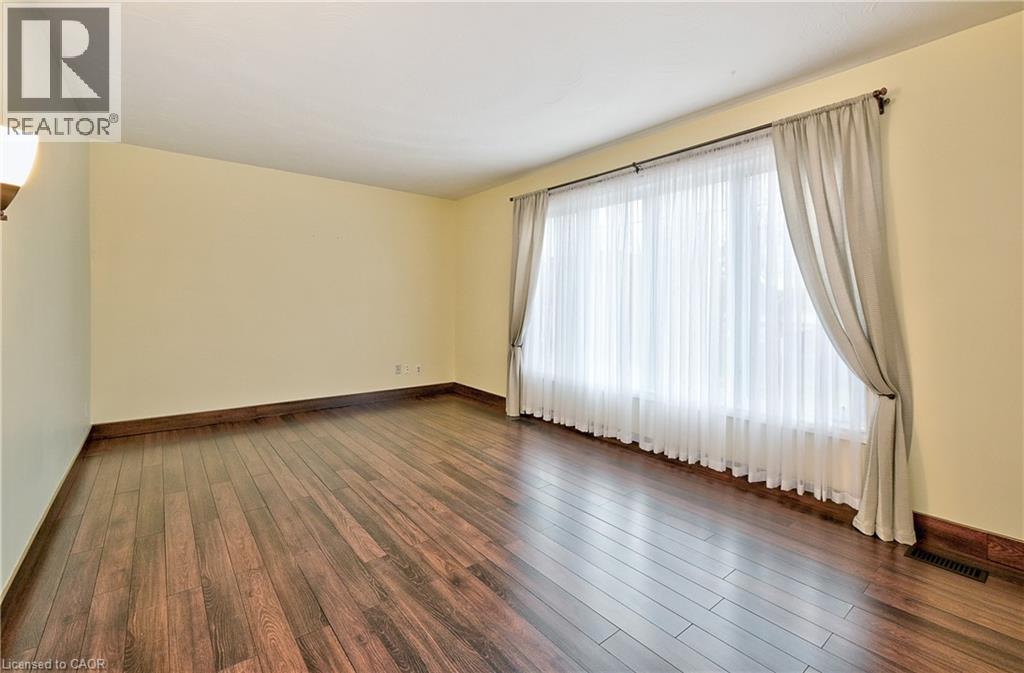 Spacious room featuring wood-finish flooring, light-colored walls, and a large window with sheer and drapery window treatments - 1476 Barton Street E, Hamilton, ON - Indoor Photo Showing Other Room