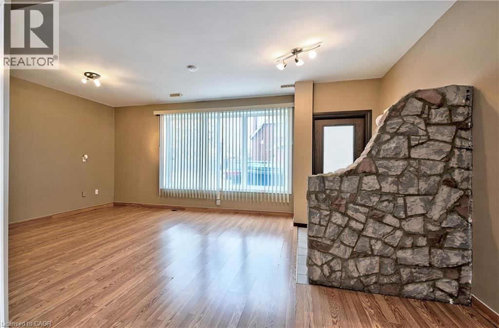 Interior space with wood-finish flooring, a prominent stone partition wall, and vertical blinds covering a large window - 1476 Barton Street E, Hamilton, ON - Indoor Photo Showing Other Room