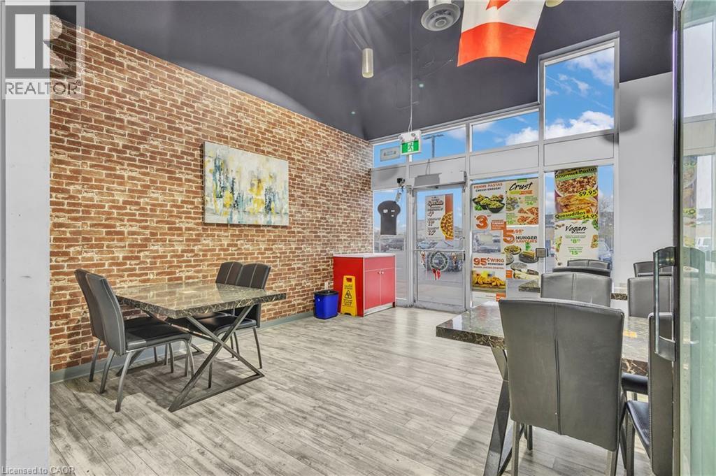 Interior space featuring an exposed brick wall, wood-finish flooring, and expansive storefront windows - 545 Hespeler Road, Cambridge, ON