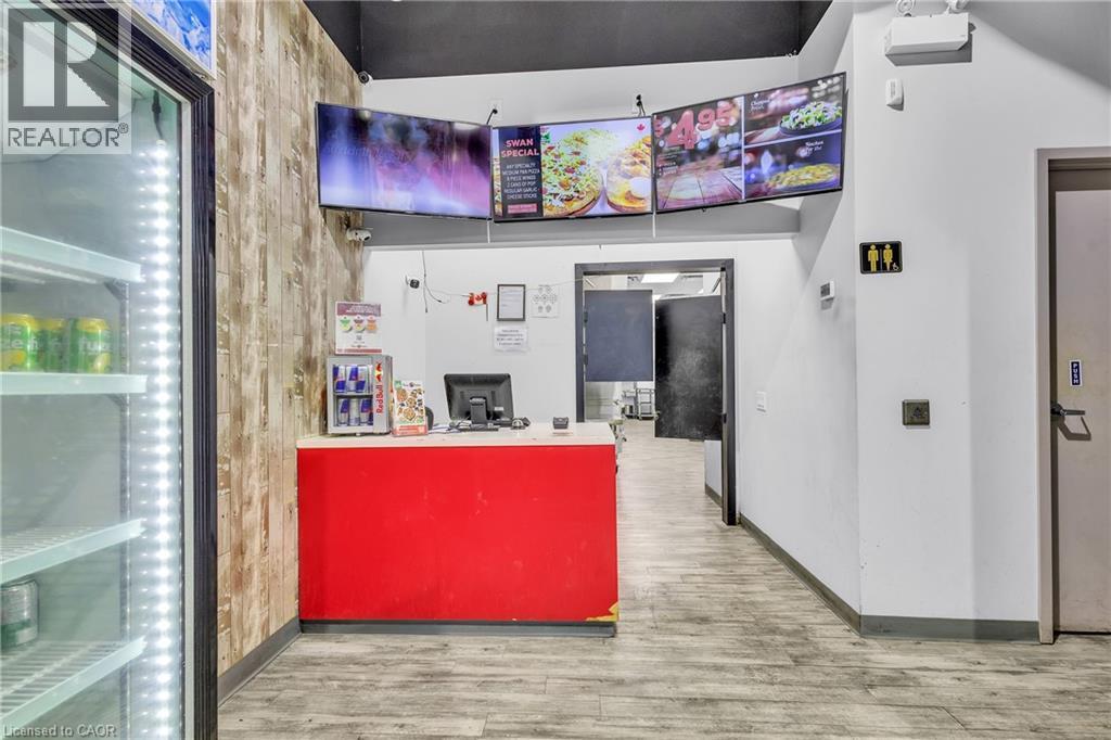 Reception area featuring a red service counter with a light-toned countertop, wood-finish accent wall, and wood-finish flooring - 545 Hespeler Road, Cambridge, ON