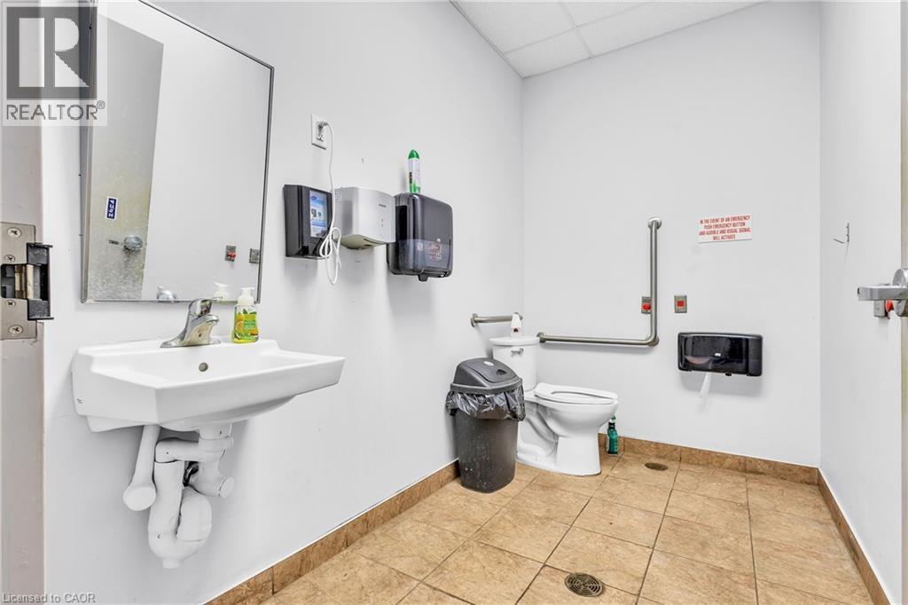 Restroom featuring a wall-mounted sink with a chrome faucet, a toilet with grab bars, and light-toned tile flooring - 545 Hespeler Road, Cambridge, ON