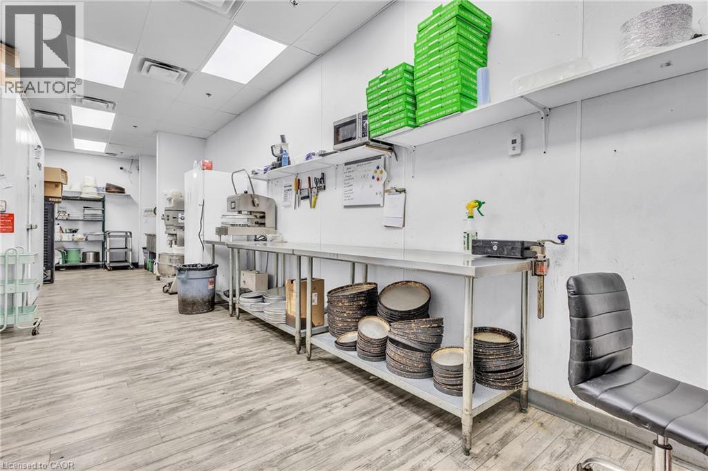 Commercial kitchen space featuring light wood-finish flooring, white panel walls, and multiple stainless steel prep tables - 545 Hespeler Road, Cambridge, ON