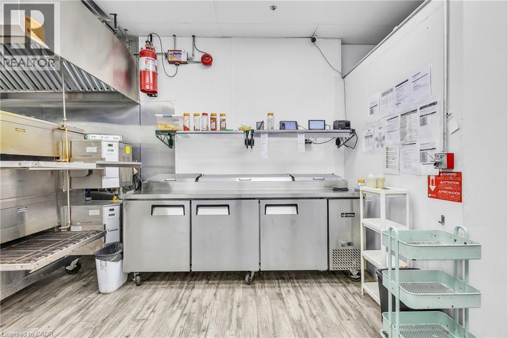 Commercial kitchen workspace featuring stainless steel appliances, a large exhaust hood, and light wood-finish flooring - 545 Hespeler Road, Cambridge, ON