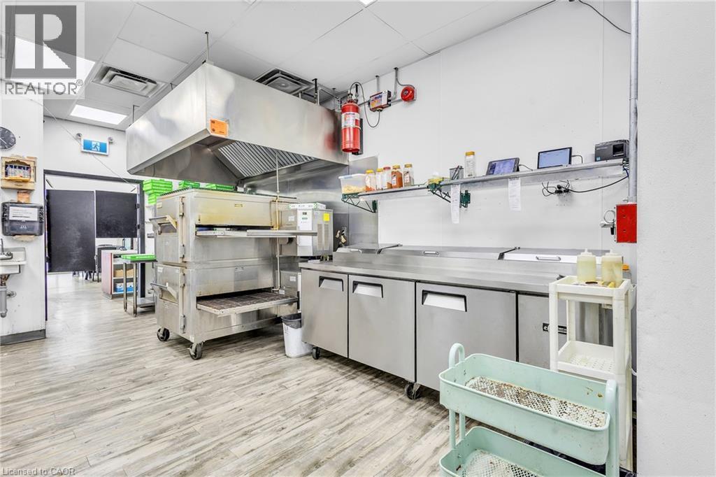 Commercial kitchen featuring stainless steel appliances, a large exhaust hood system, and wood-finish flooring - 545 Hespeler Road, Cambridge, ON
