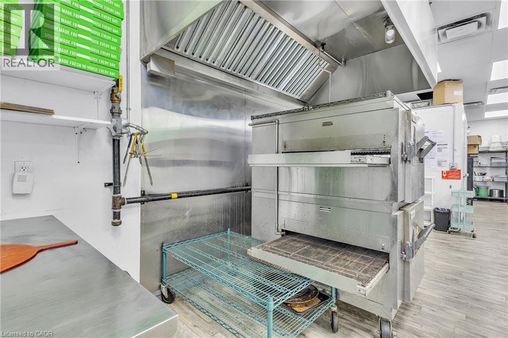 Commercial kitchen featuring stainless steel appliances, a large exhaust hood, metal shelving, and wood-finish flooring - 545 Hespeler Road, Cambridge, ON