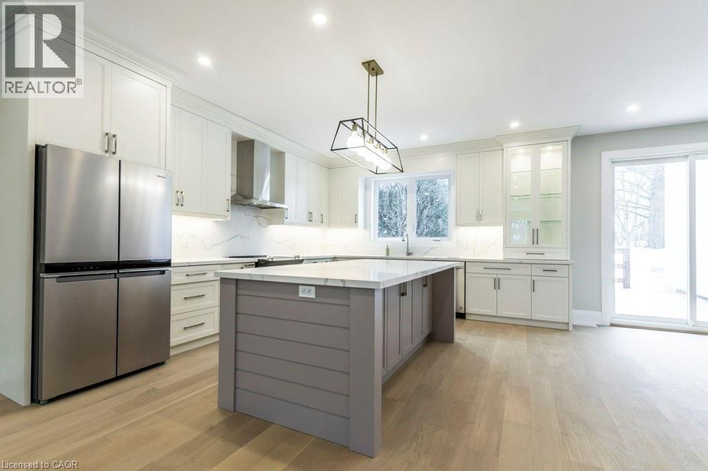 Dual tone kitchen featuring freestanding refrigerator, decorative backsplash, dual tone cabinets, light wood-type flooring, and a kitchen island - 1105 Main Street E, Cambridge, ON - Indoor Photo Showing Kitchen With Stainless Steel Kitchen With Upgraded Kitchen