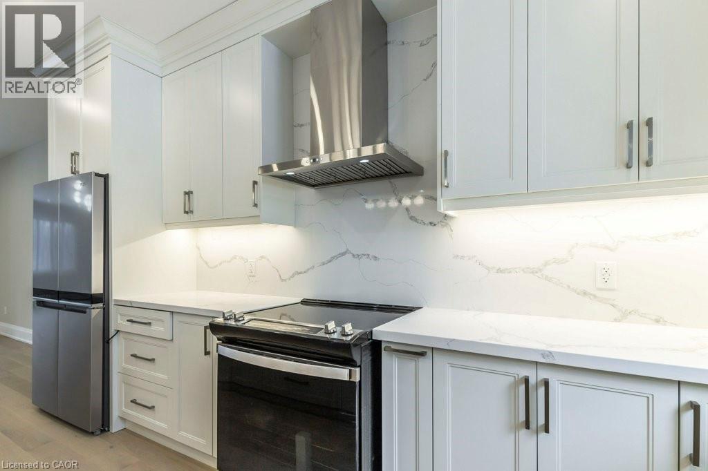 Kitchen featuring stainless steel appliances, decorative backsplash, light stone counters, light wood finished floors, and white cabinets - 1105 Main Street E, Cambridge, ON - Indoor Photo Showing Kitchen With Upgraded Kitchen