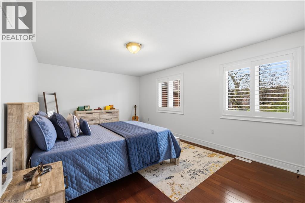 Bright interior space featuring two windows with white plantation shutters, rich wood-finish flooring, and crisp white walls - 199 Hunter Street W, Hamilton, ON - Indoor Photo Showing Bedroom