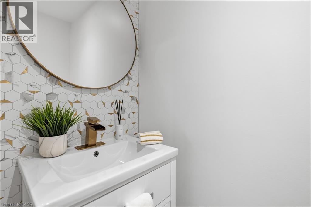 White vanity with integrated sink, brass waterfall faucet, and round brass-framed mirror - 199 Hunter Street W, Hamilton, ON - Indoor Photo Showing Bathroom