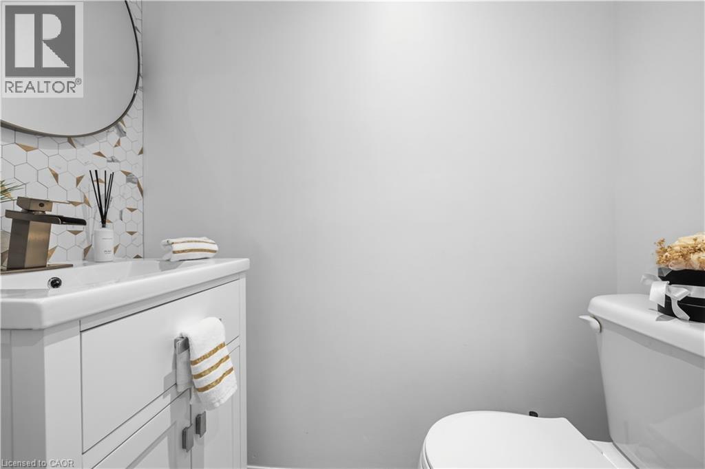 White vanity with integrated sink, brass-tone faucet, and round mirror - 199 Hunter Street W, Hamilton, ON - Indoor Photo Showing Bathroom