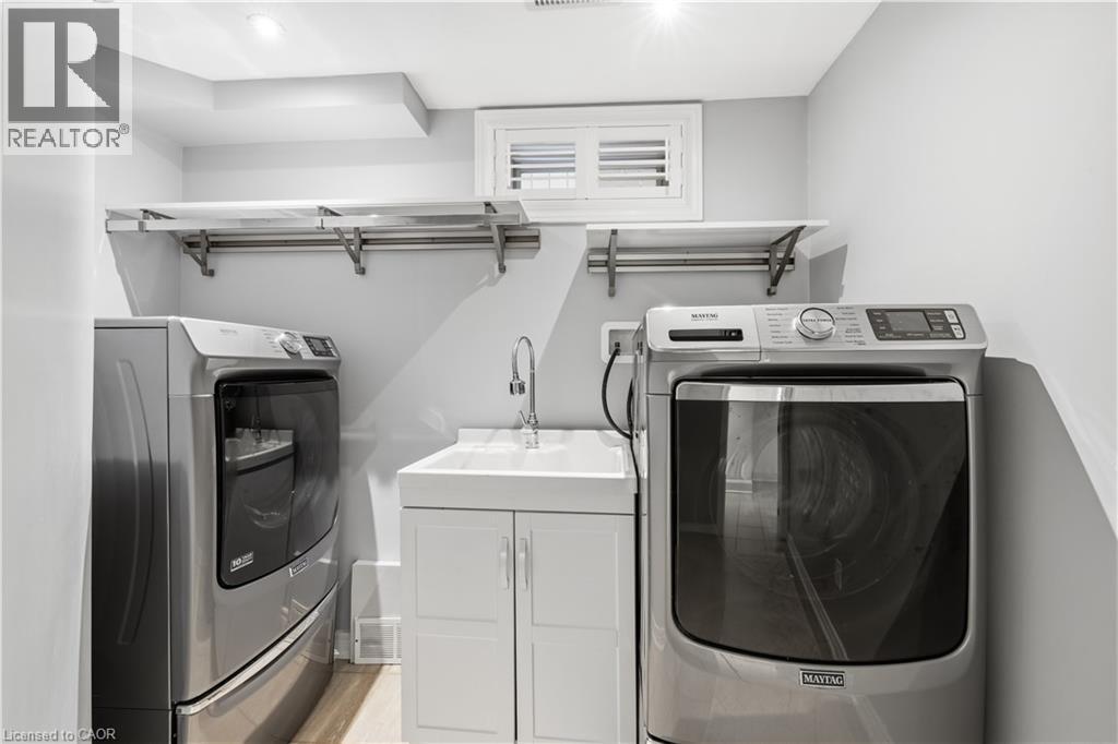 Dedicated utility space featuring a laundry sink with a chrome faucet, white cabinetry, and overhead shelving with a hanging rod - 199 Hunter Street W, Hamilton, ON - Indoor Photo Showing Laundry Room