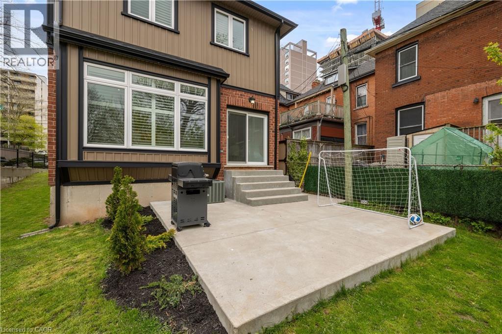 Rear exterior featuring a concrete patio, sliding glass door, and multiple windows with blinds - 199 Hunter Street W, Hamilton, ON - Outdoor