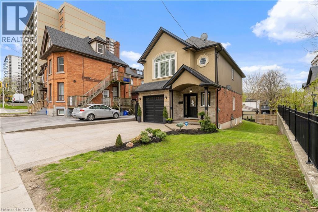 Contemporary stucco and brick exterior featuring a single-car garage, covered entry with a dark-paneled door, and a circular window accent - 199 Hunter Street W, Hamilton, ON - Outdoor