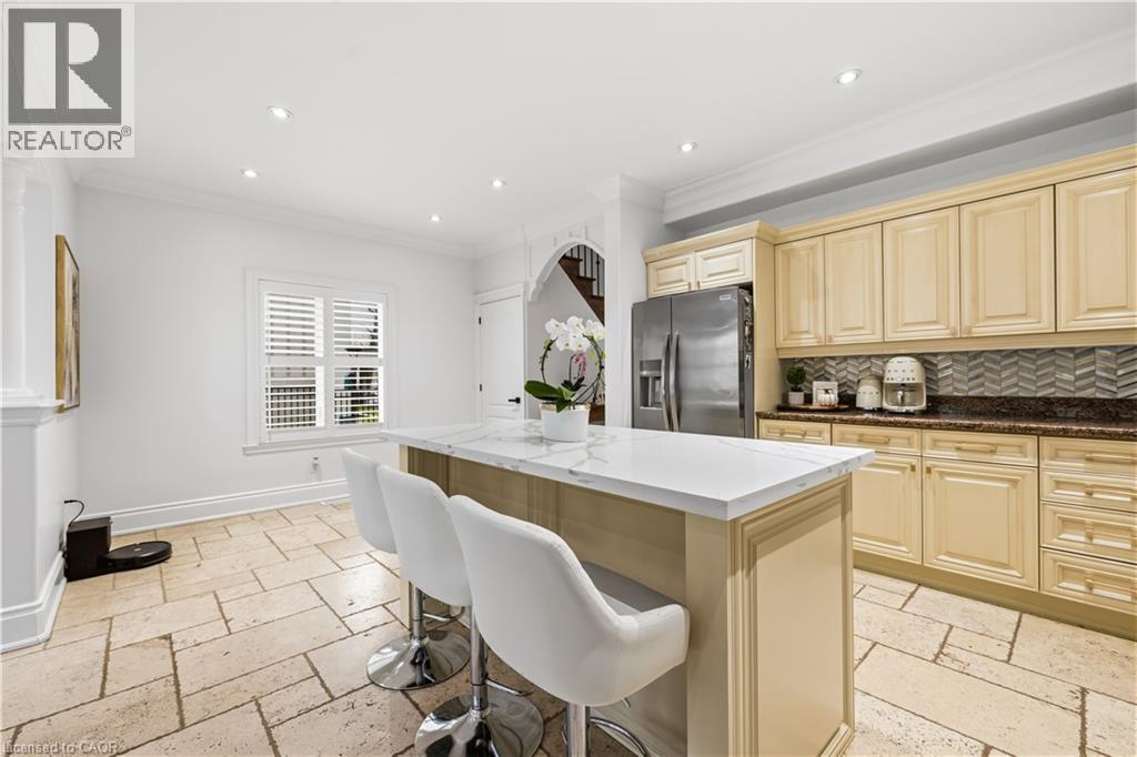 Kitchen featuring a central island with a white countertop, beige cabinetry, stainless steel refrigerator, patterned tile backsplash, and light-toned tile flooring - 199 Hunter Street W, Hamilton, ON - Indoor Photo Showing Kitchen